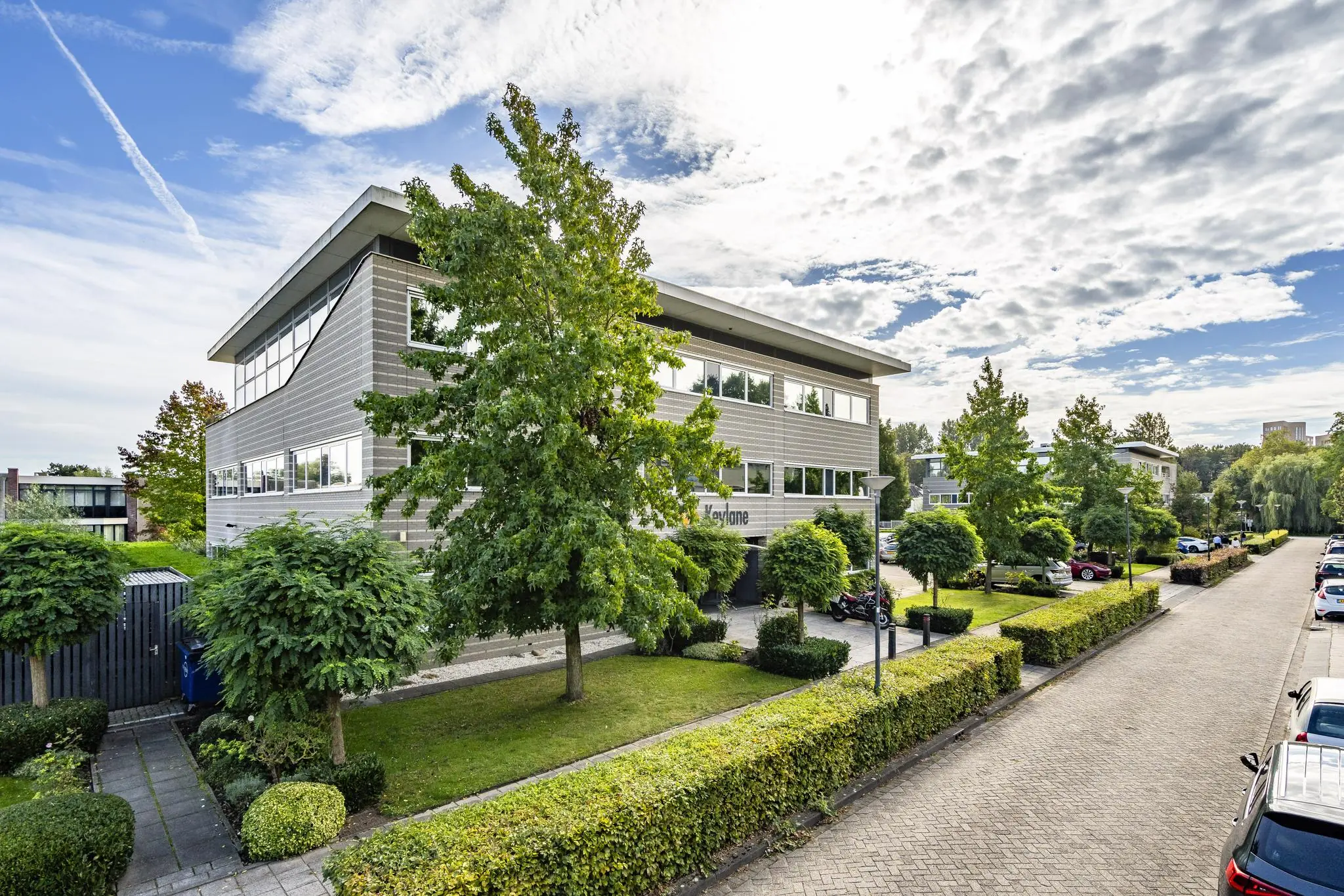Modern kantoorgebouw aan de Jan Leentvaarlaan met omliggende bomen en geparkeerde auto's op een rustige straat.